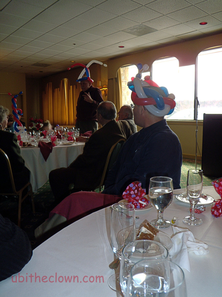 Balloon hats at an 80th birthday party. The guest of honor is speaking.
